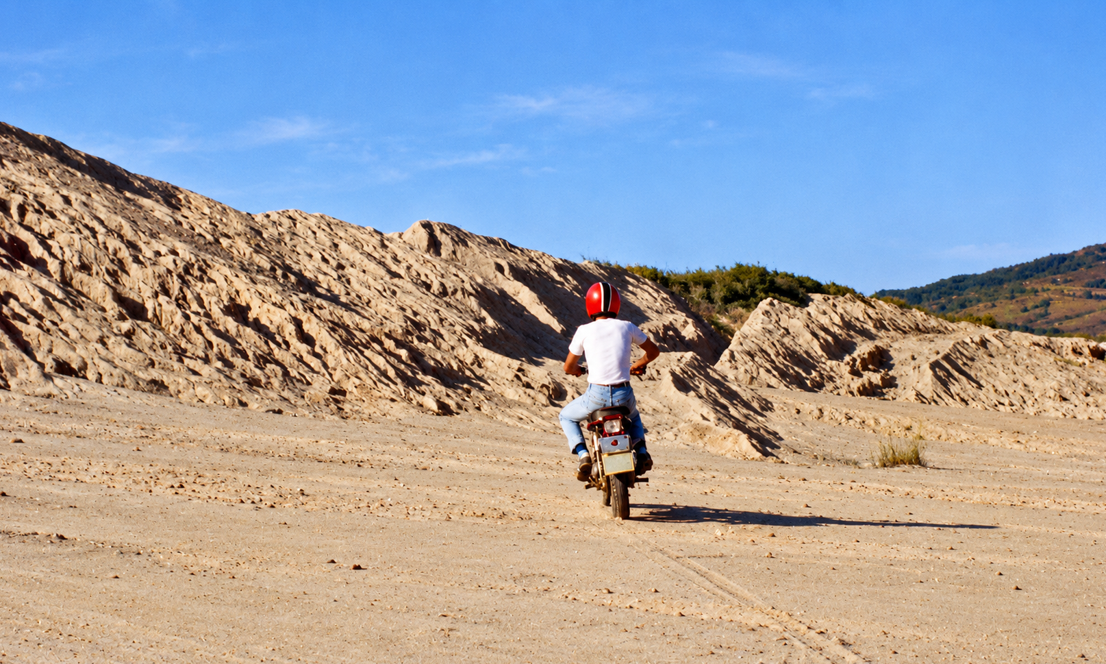 A motorcyclist wearing a red helmet riding across the sandy tailings dam.