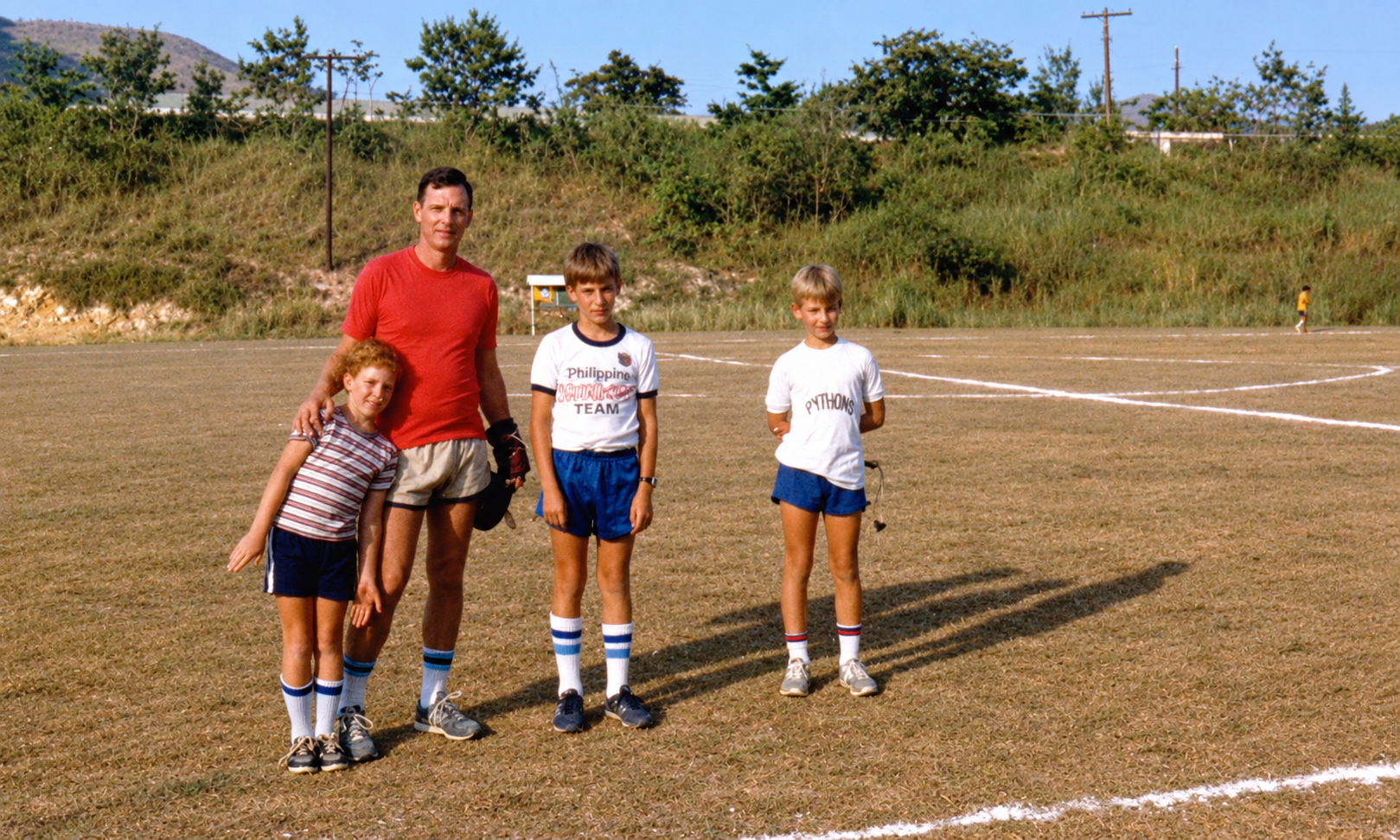A man and three boys standing together on the soccer field.