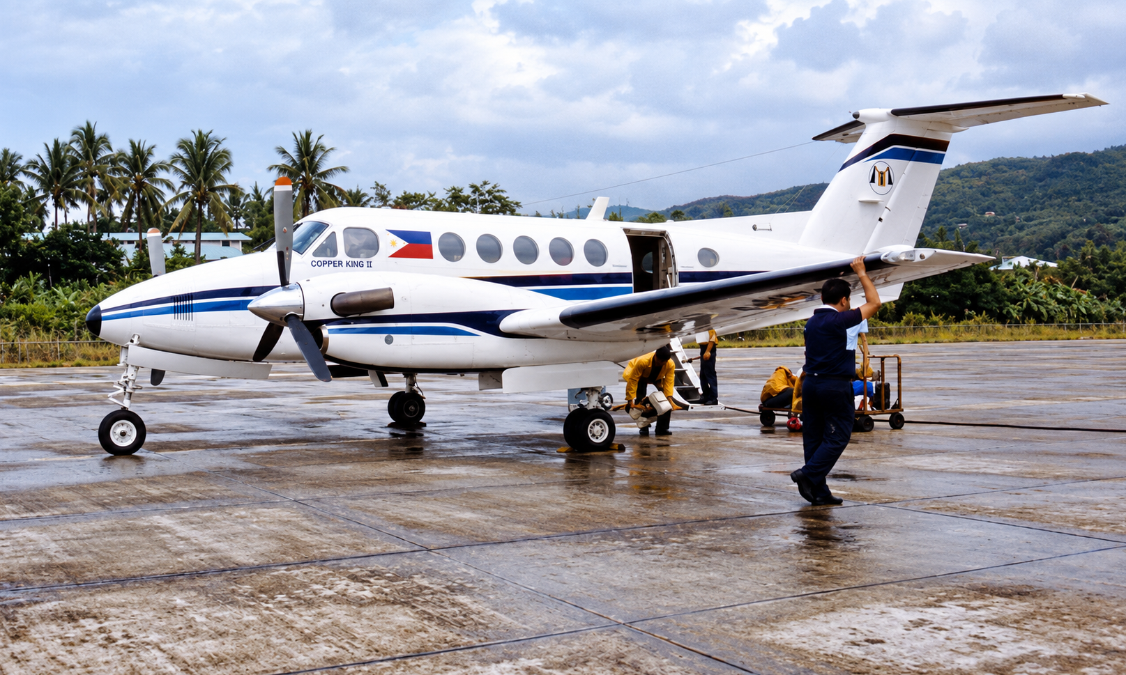 The blue-striped Copper King II plane on the apron with ground crew beside it.