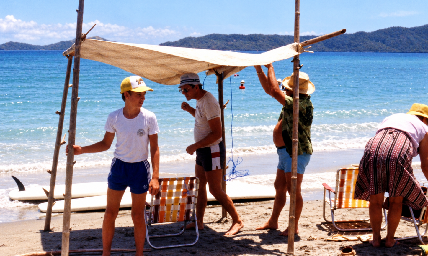 A group assembling a shade shelter beside beach chairs and windsurfing boards at the water’s edge.