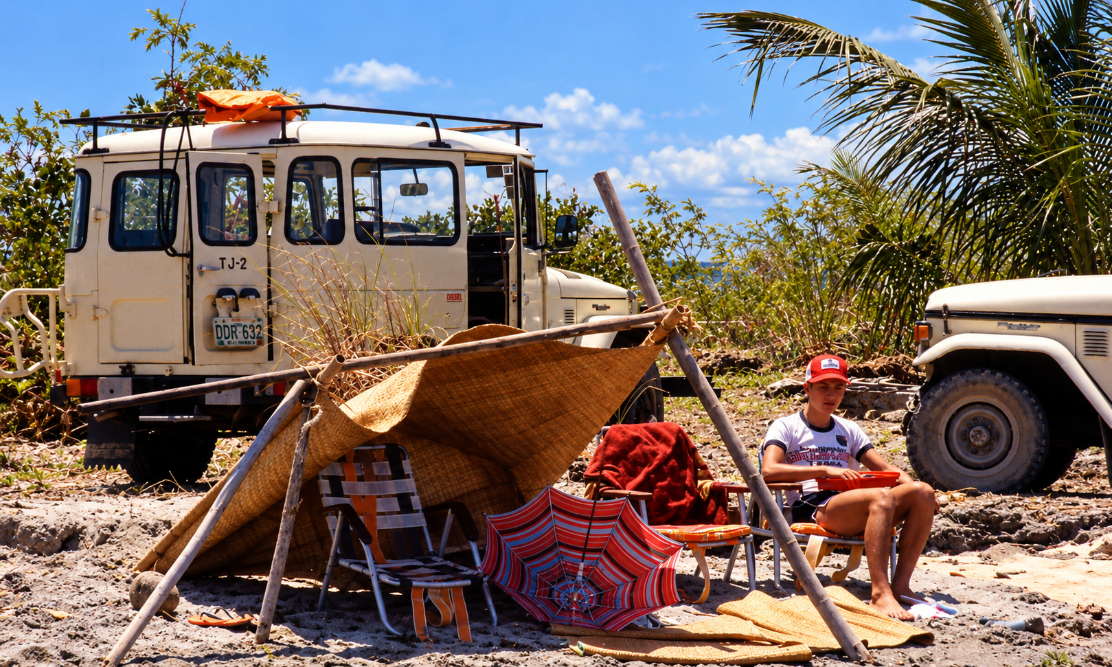 A boy seated beside a makeshift beach shelter, with two vehicles parked behind him.