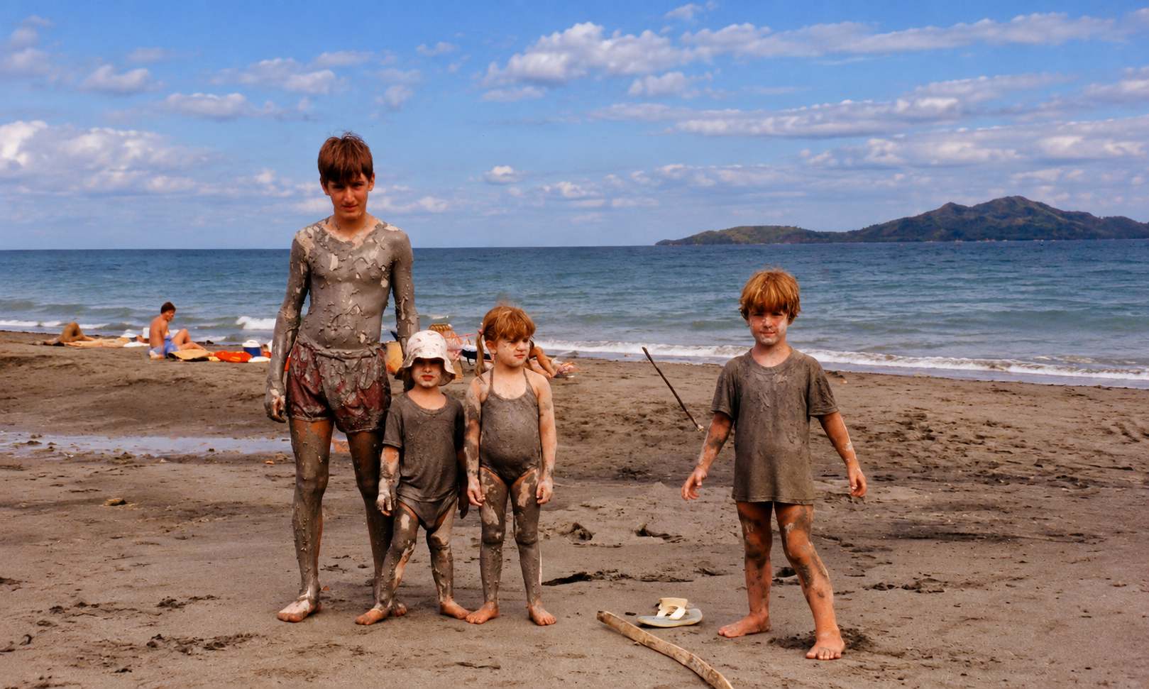 Four children covered in mud standing together on the beach.