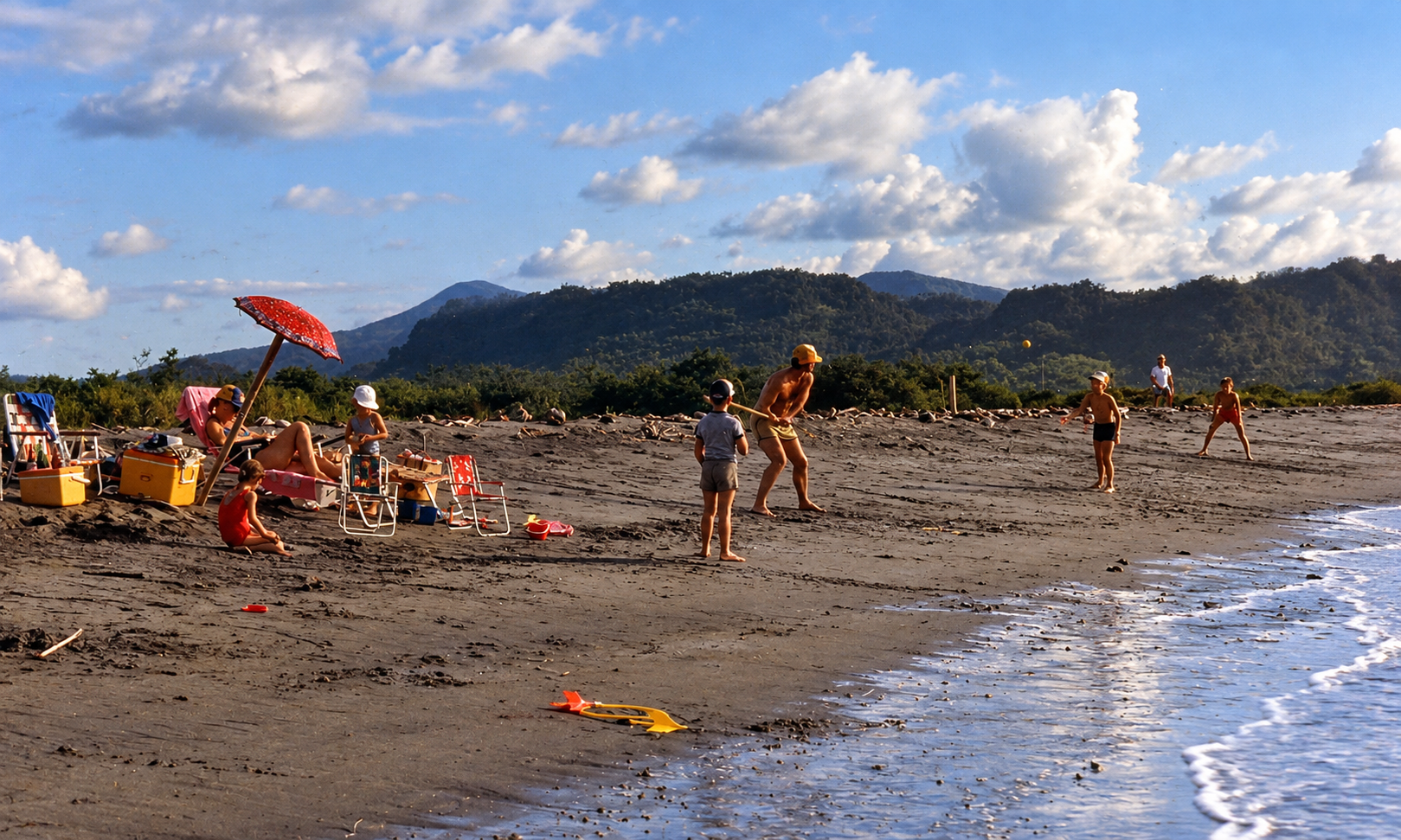 Adults and children playing ball near the shoreline beside a group of beach chairs.