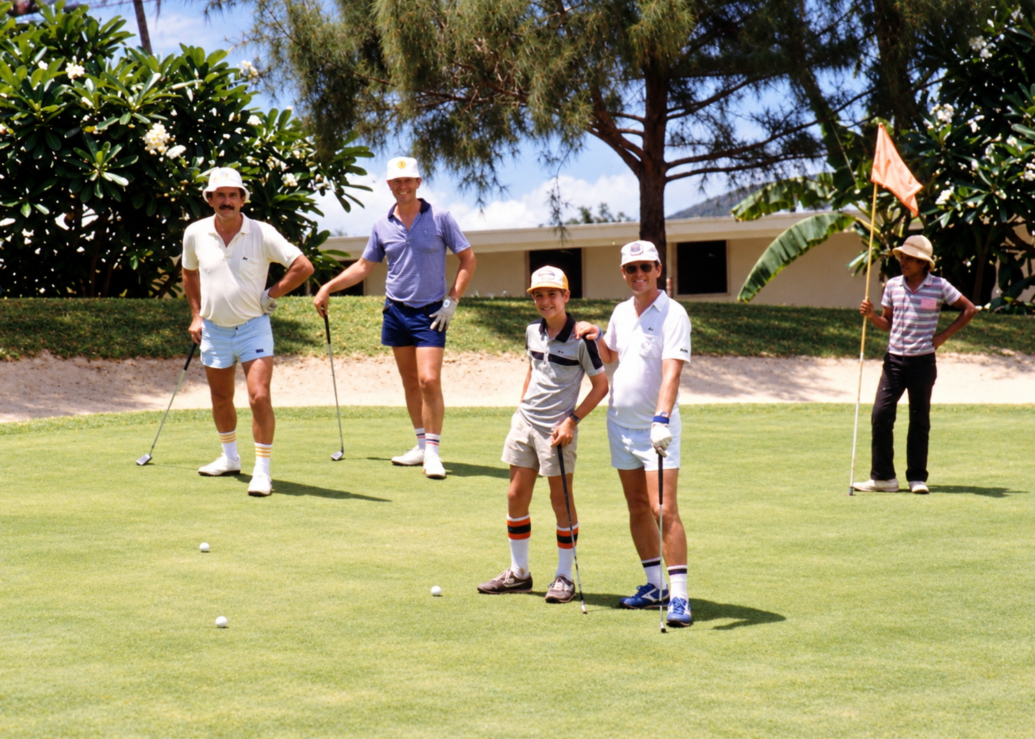 Golfers and caddies gathered on a green beside a flagstick and sand trap.