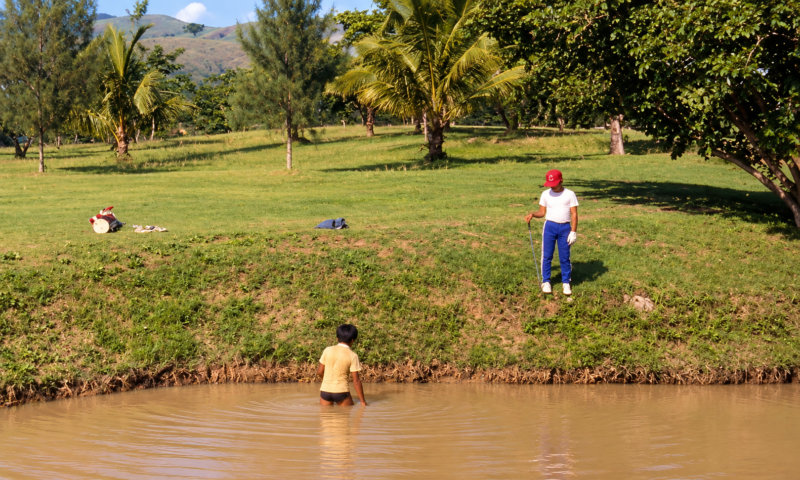 A golfer beside a pond while another person stands in the water.