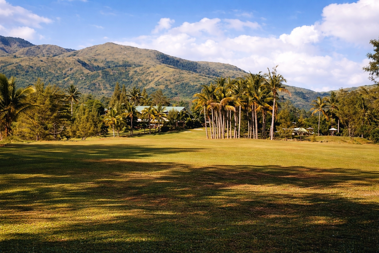 Marcopper Golf Course, with its sunlit fairway, tall palms, clubhouse, and green mountains beneath a blue sky.