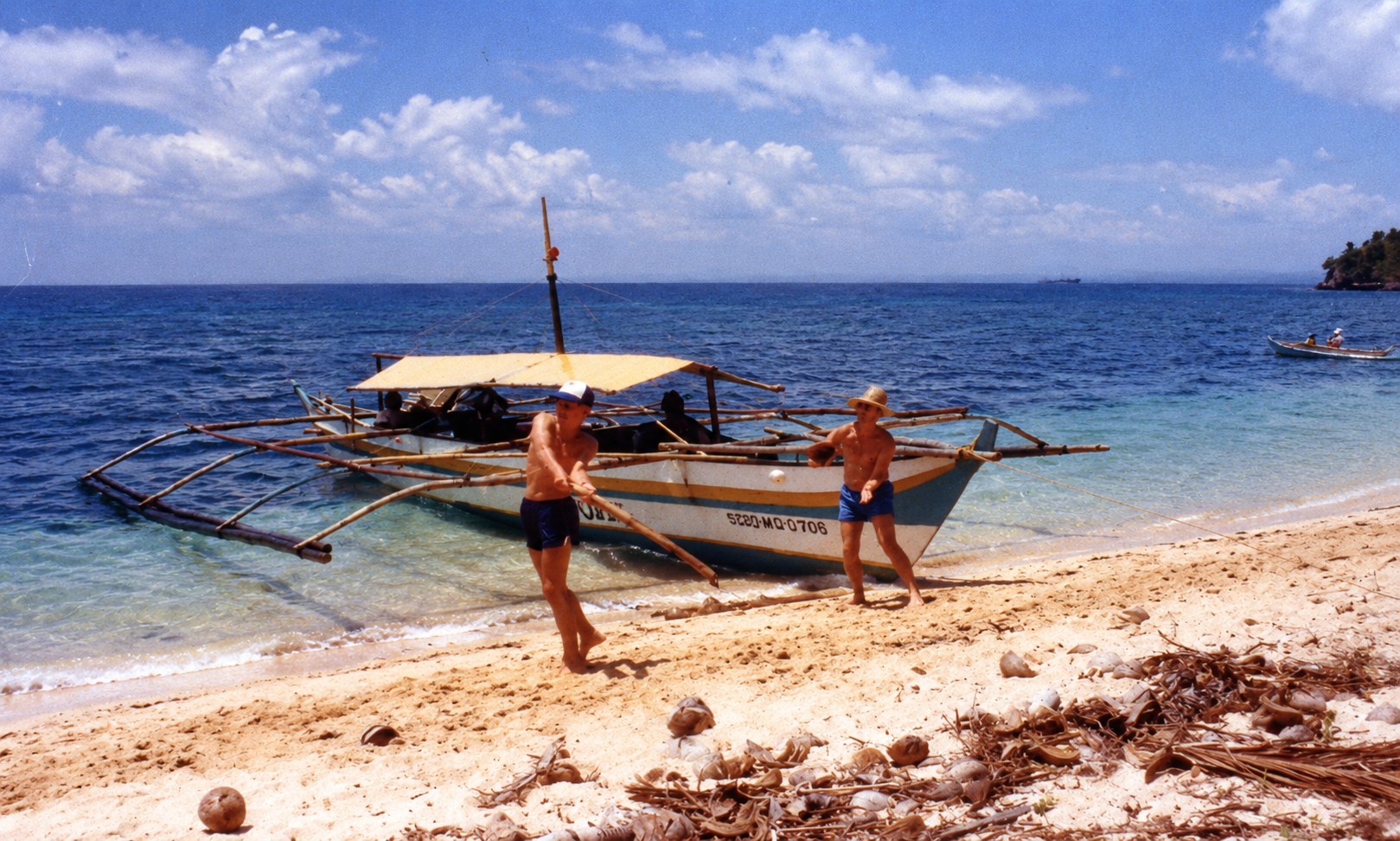 Two boys playing ball on the shore beside an outrigger boat.
