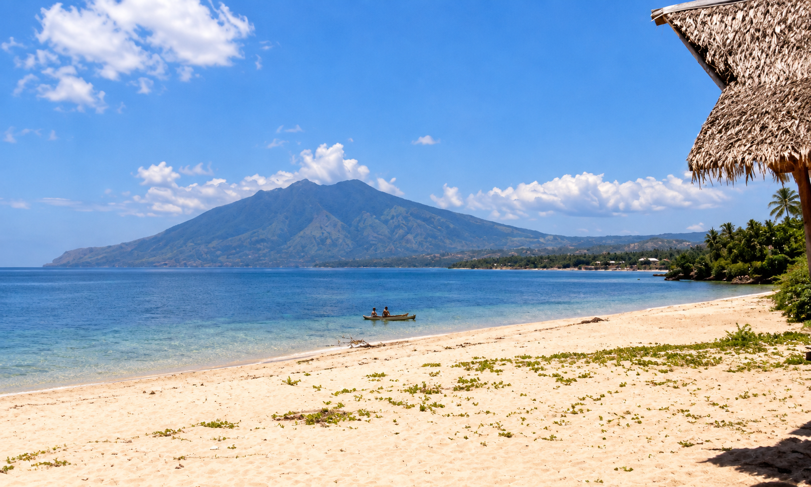 A white sand beach overlooking a blue bay and mountain, with a canoe near the water.