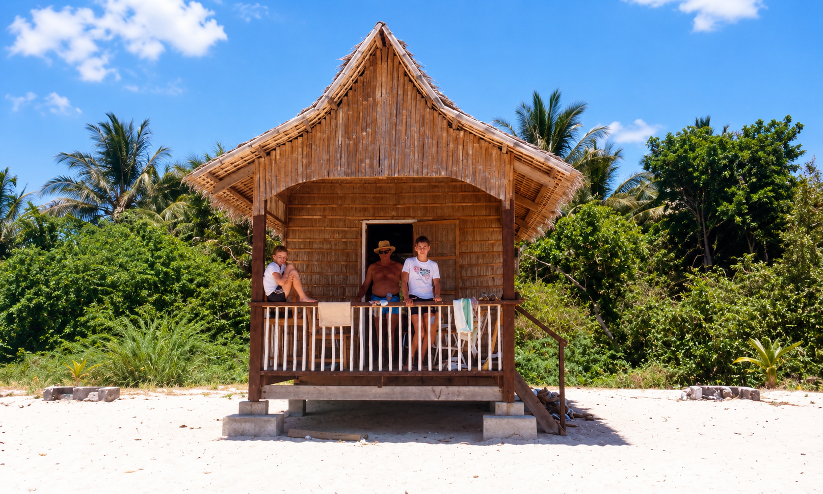 Three people relaxing on the porch of a bamboo beach hut.
