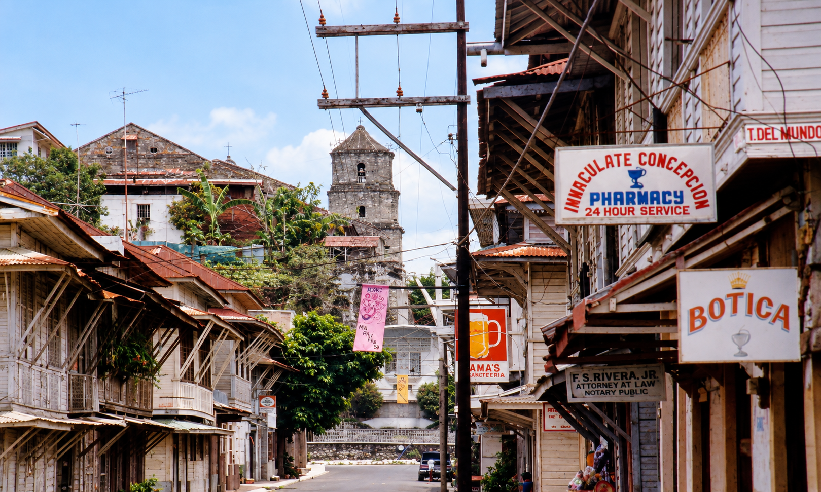 An old commercial street with wooden buildings, pharmacy signs, and a church bell tower.