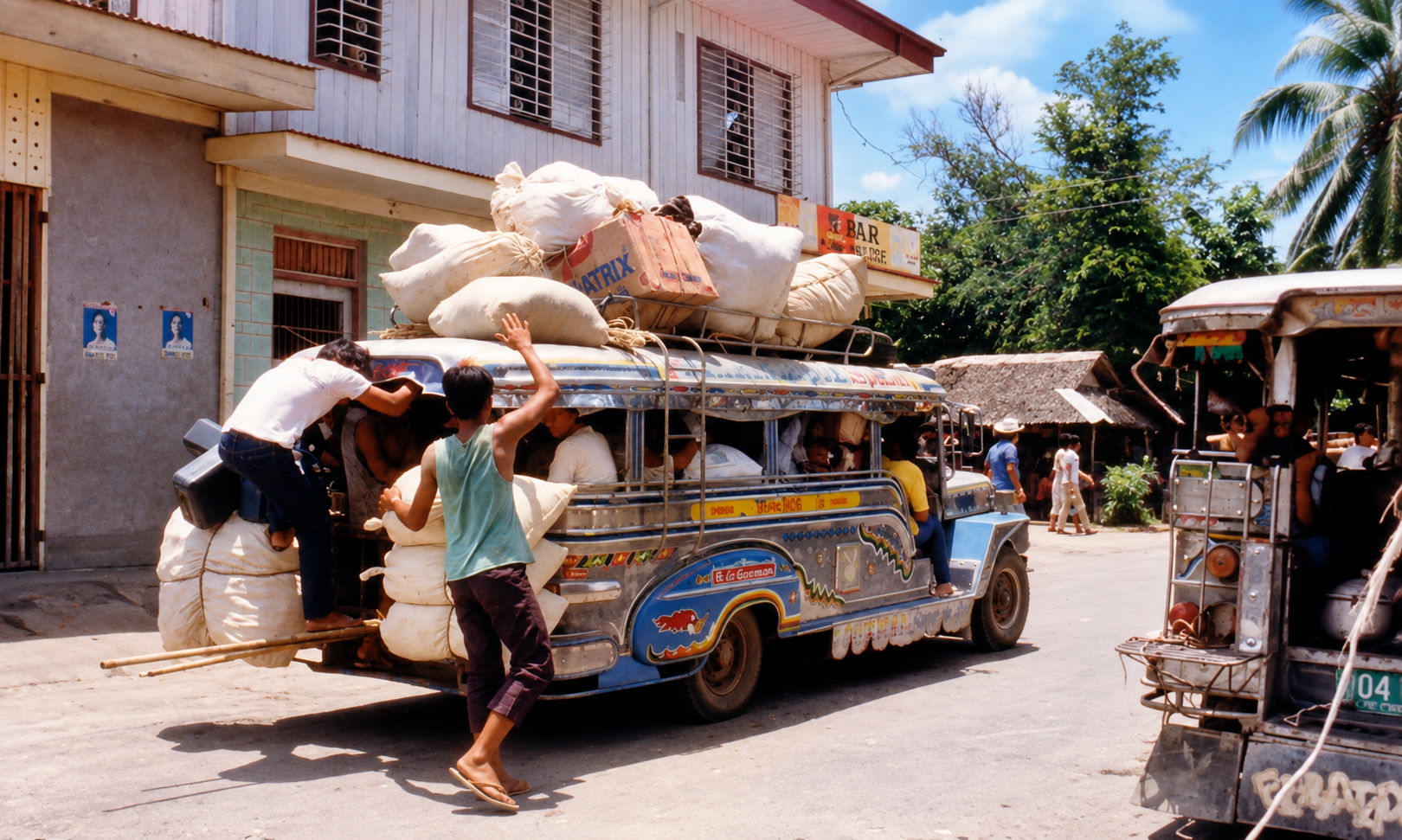 Passengers boarding a jeepney loaded with sacks on its roof and rear step.