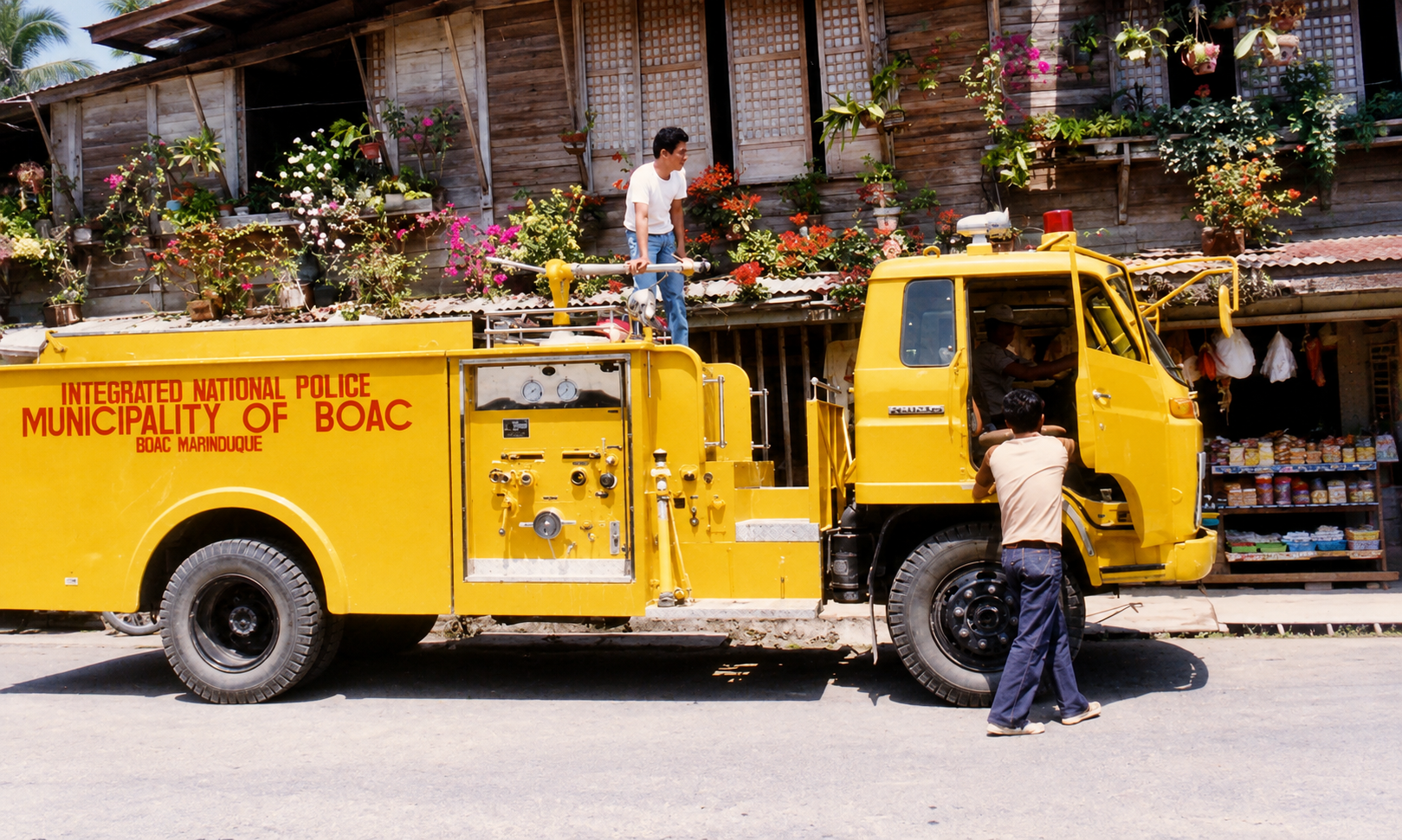 A bright yellow Municipality of Boac fire truck parked beside a wooden building with flowers.