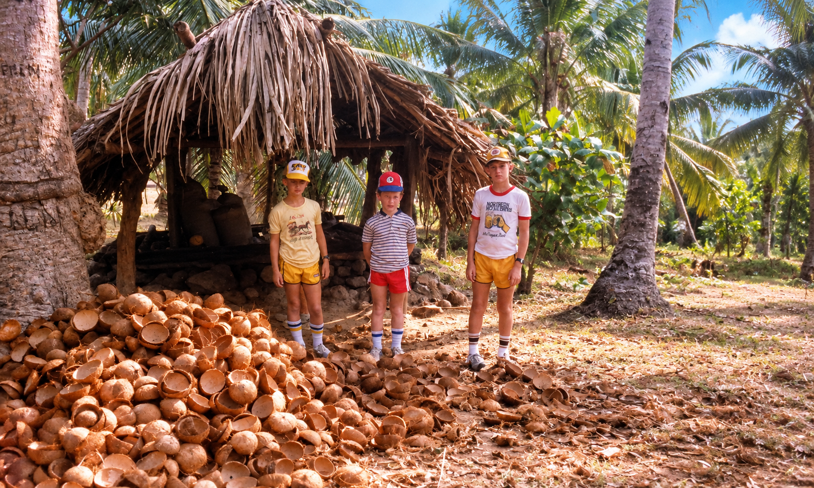 Three boys beside a thatched hut and a pile of coconut shells.