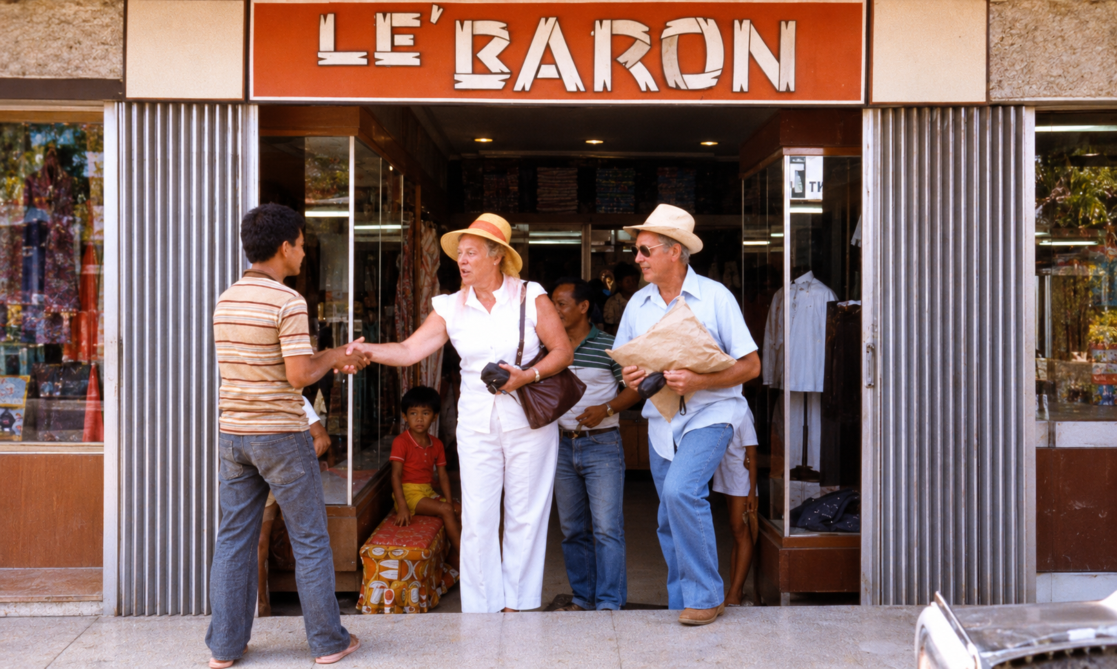 A woman shaking hands outside the Le’ Baron shop beside a man holding a parcel.