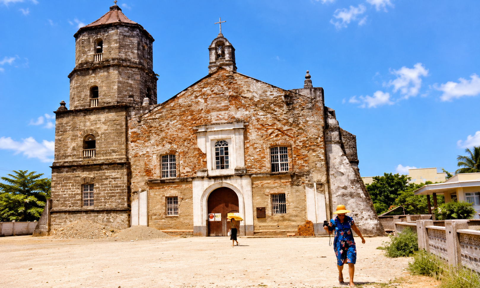 A stone and brick church with a bell tower and a woman in a yellow hat in the foreground.
