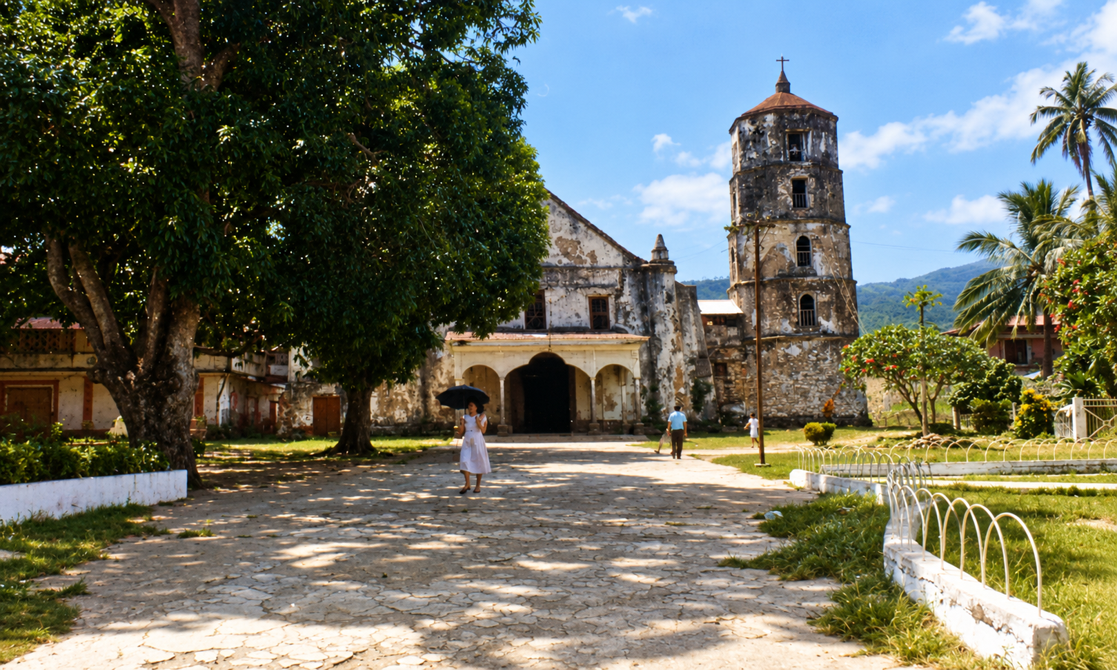 An old church and bell tower beyond a stone path shaded by a large tree.