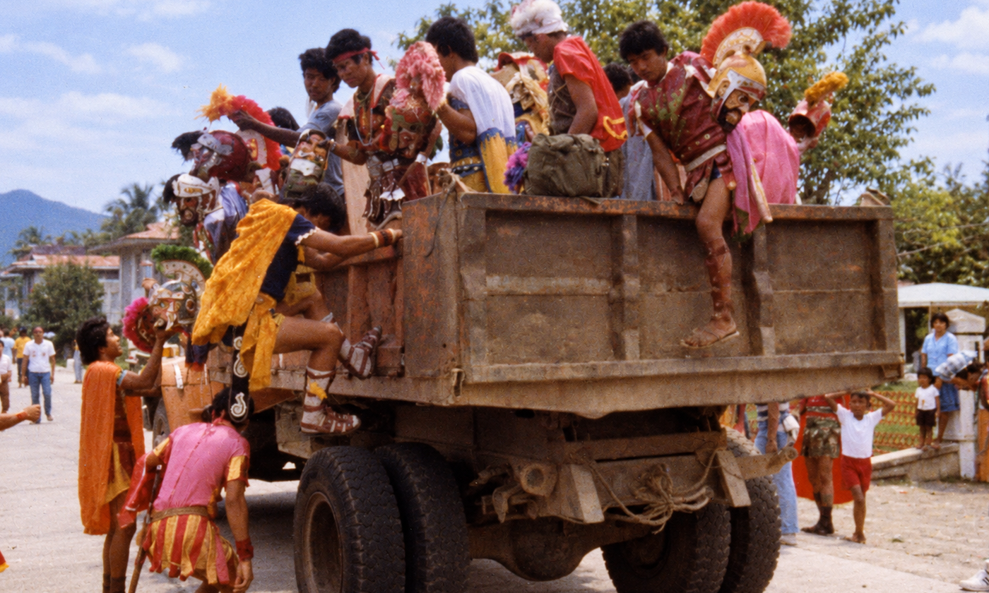 Moriones festival participants in colorful costumes climbing onto and riding in a truck.