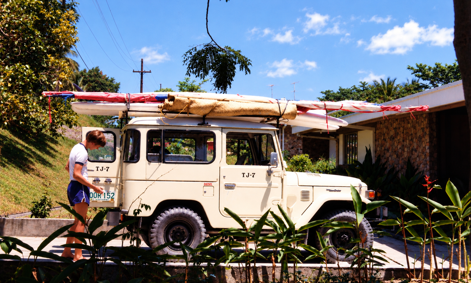 A boy beside the cream Land Cruiser, loaded with windsurfing boards outside the house.