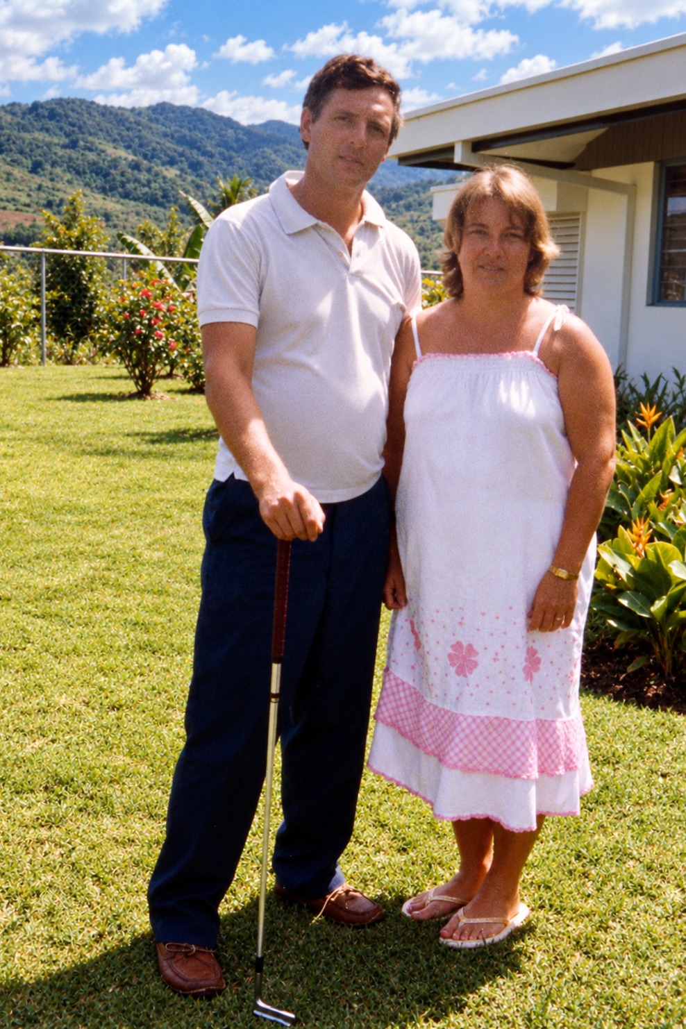 A man holding a golf club and a woman standing together on the lawn outside the house.