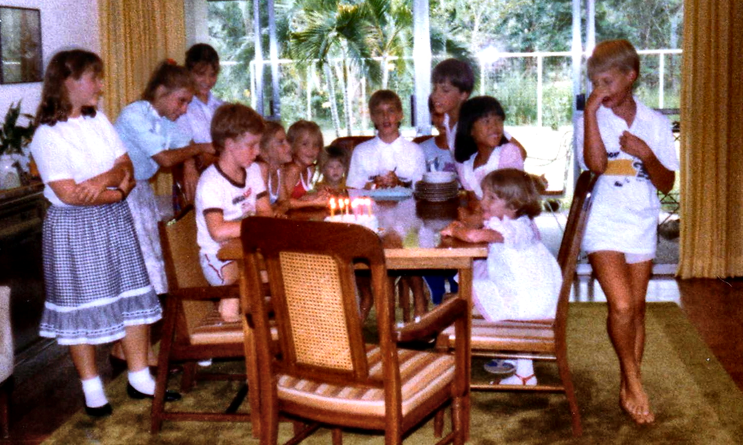 Children gathered around a birthday cake on the dining table.
