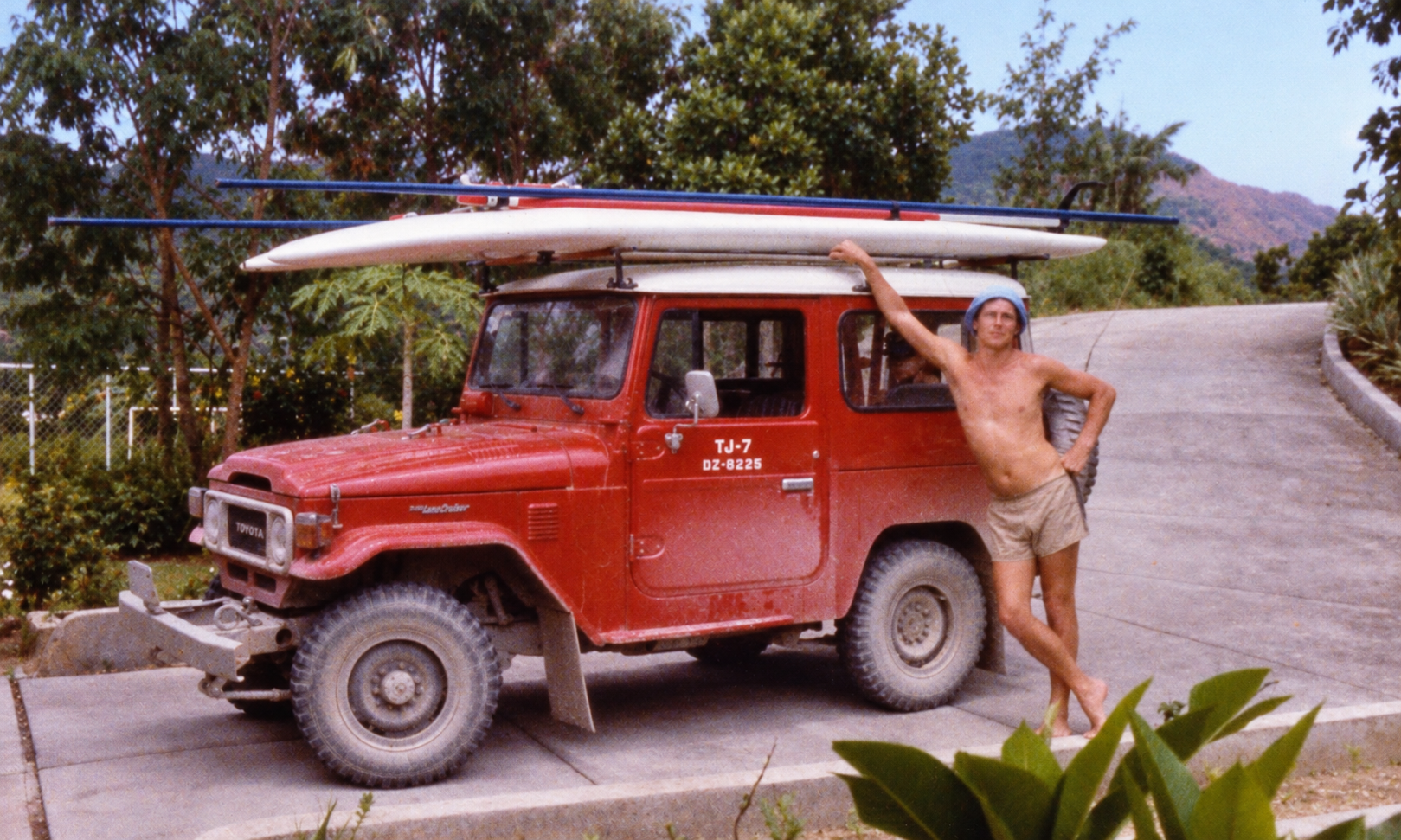 A man standing beside a red Land Cruiser carrying windsurfing boards in the driveway.
