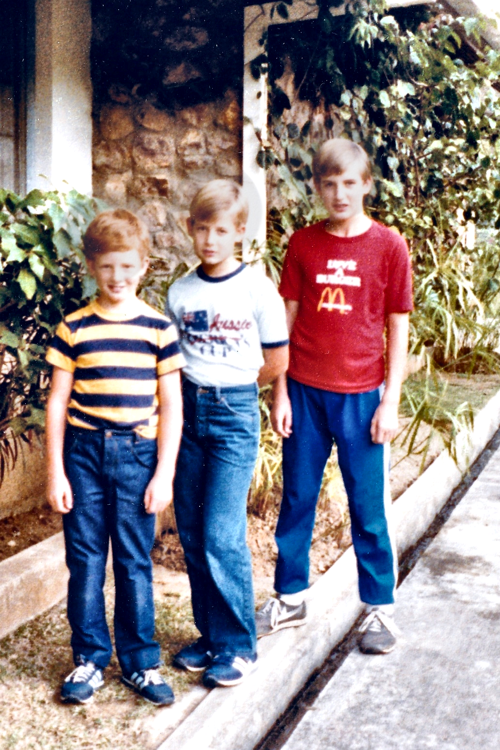 Three boys standing together on the path beside the house.
