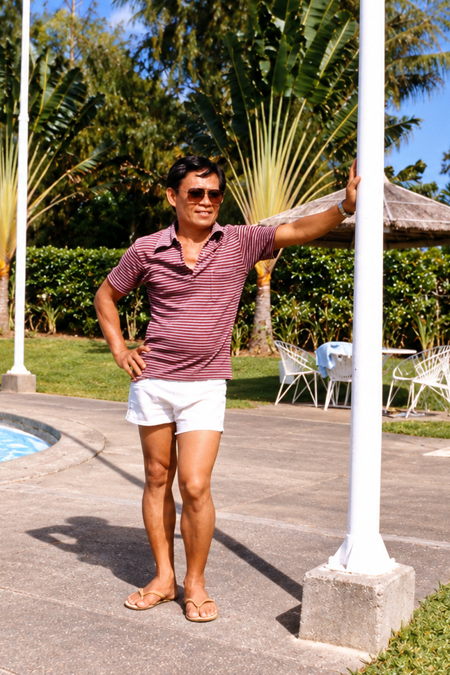 A man in sunglasses and a striped shirt standing beside a white pole at the swimming pool.