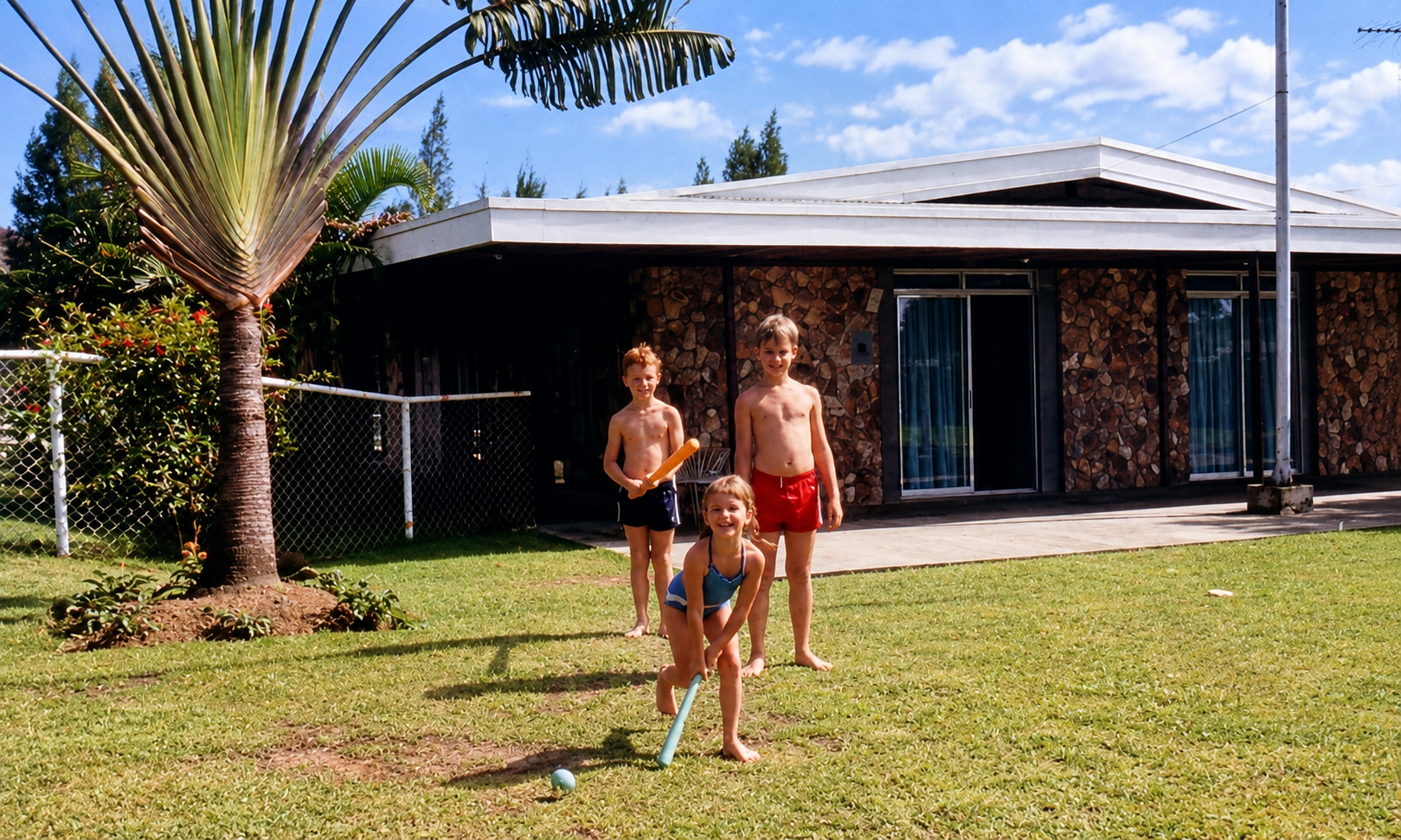 Three children playing with plastic bats and a ball on the lawn beside the stone-faced clubhouse.