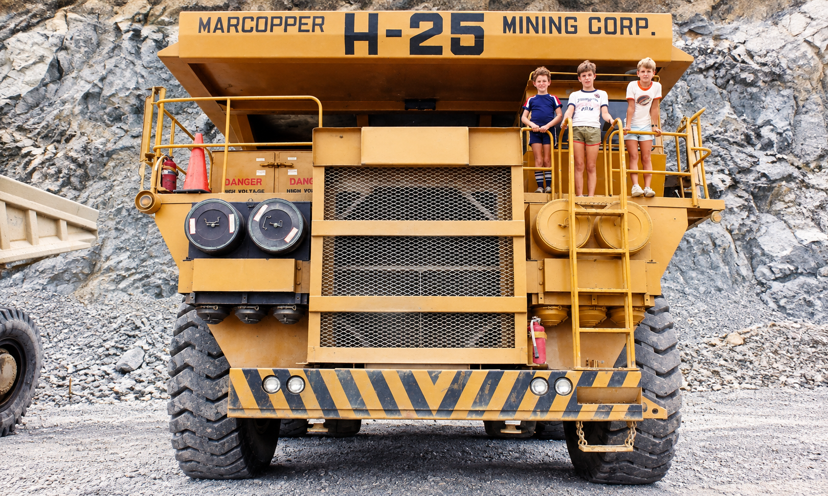 The three Trent boys standing on the platform of a towering yellow Marcopper H-25 haul truck, with a rocky mine wall behind them.