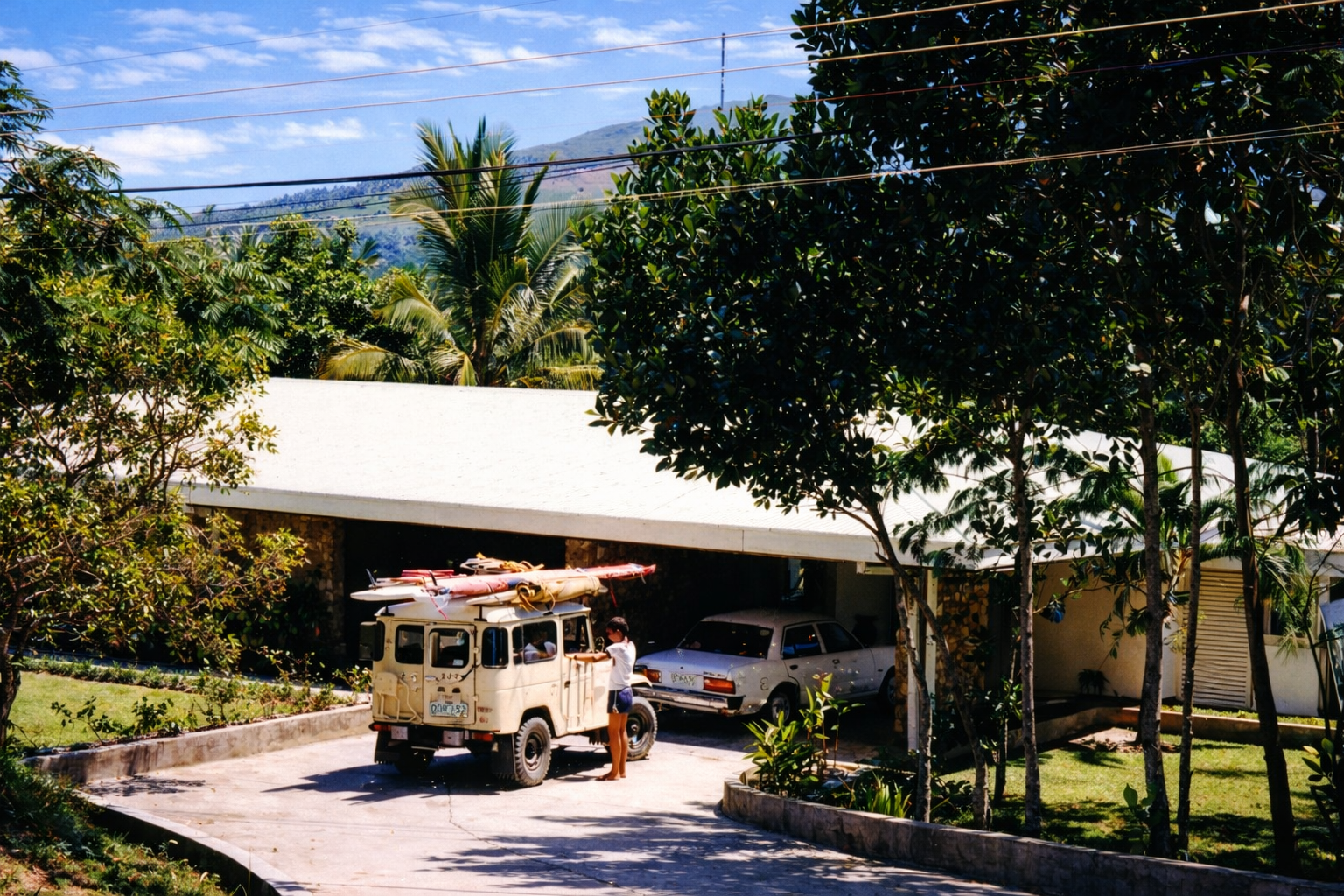 The Trent family home shaded by tropical trees, with a white vehicle carrying boards on its roof in the driveway.